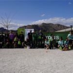 Participantes del evento con sus perros posando en las instalaciones de Argos Adiestramiento Canino, con montañas al fondo y banners de patrocinadores